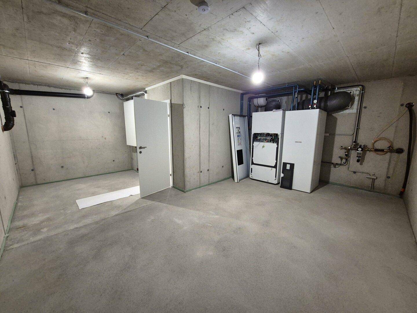 Technikraum im Keller mit Heizungsanlagen und Betonwänden.