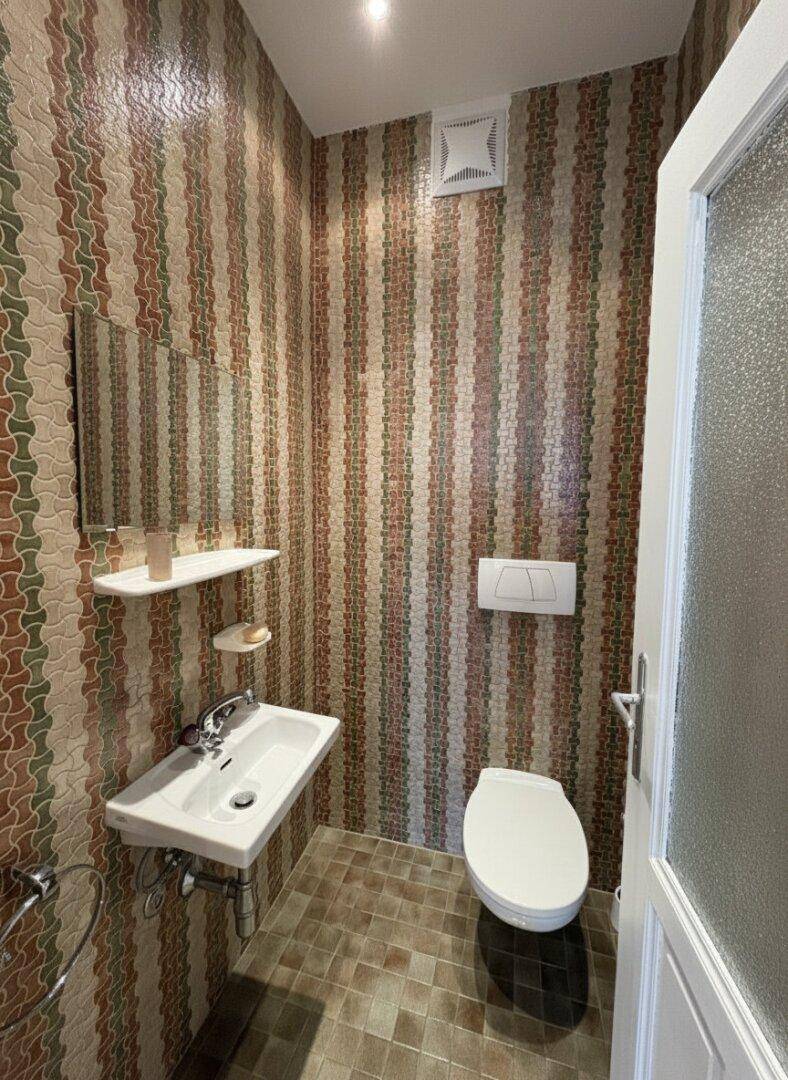 Gäste-WC mit gemusterten Fliesen, Waschbecken und wandhängender Toilette.