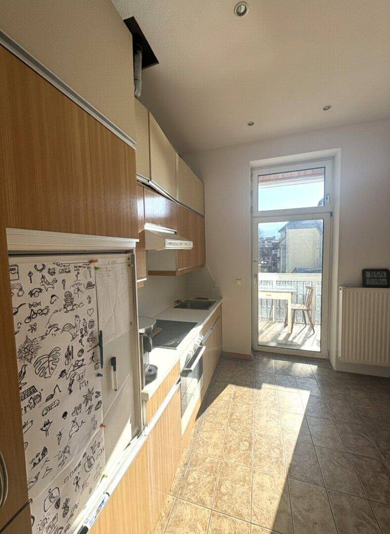 Küche mit Holzschränken, Fliesenboden und Zugang zu einem kleinen Balkon.