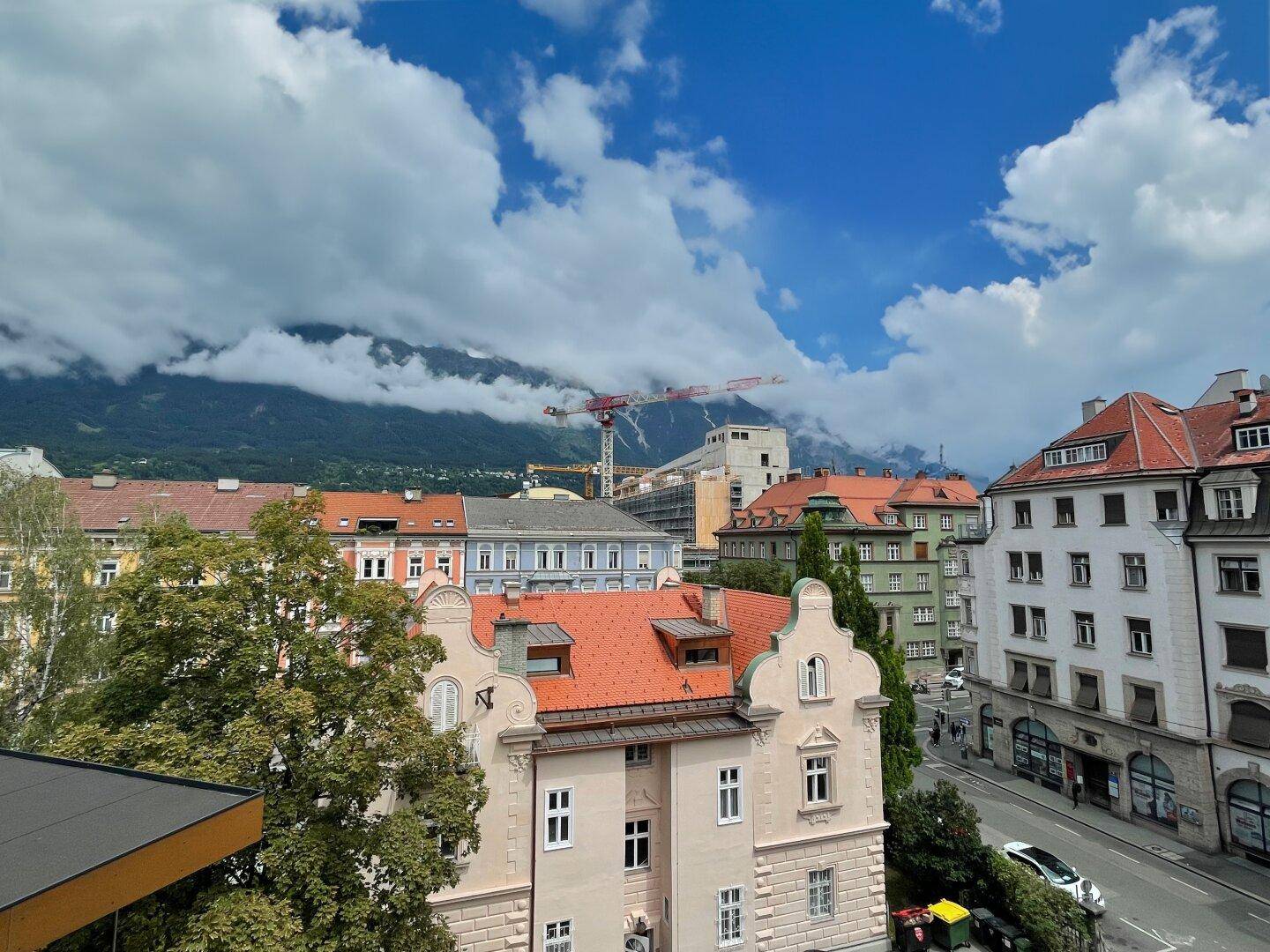 Panoramablick über die Dächer der Stadt mit majestätischen Bergen im Hintergrund und einer belebten Straße.