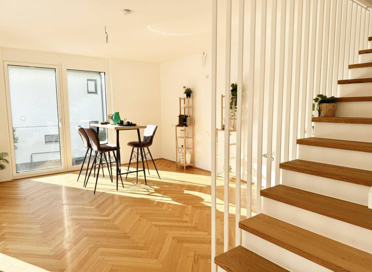 Heller Wohn- und Essbereich mit Holztreppe, Fischgrätparkett und viel Tageslicht.
