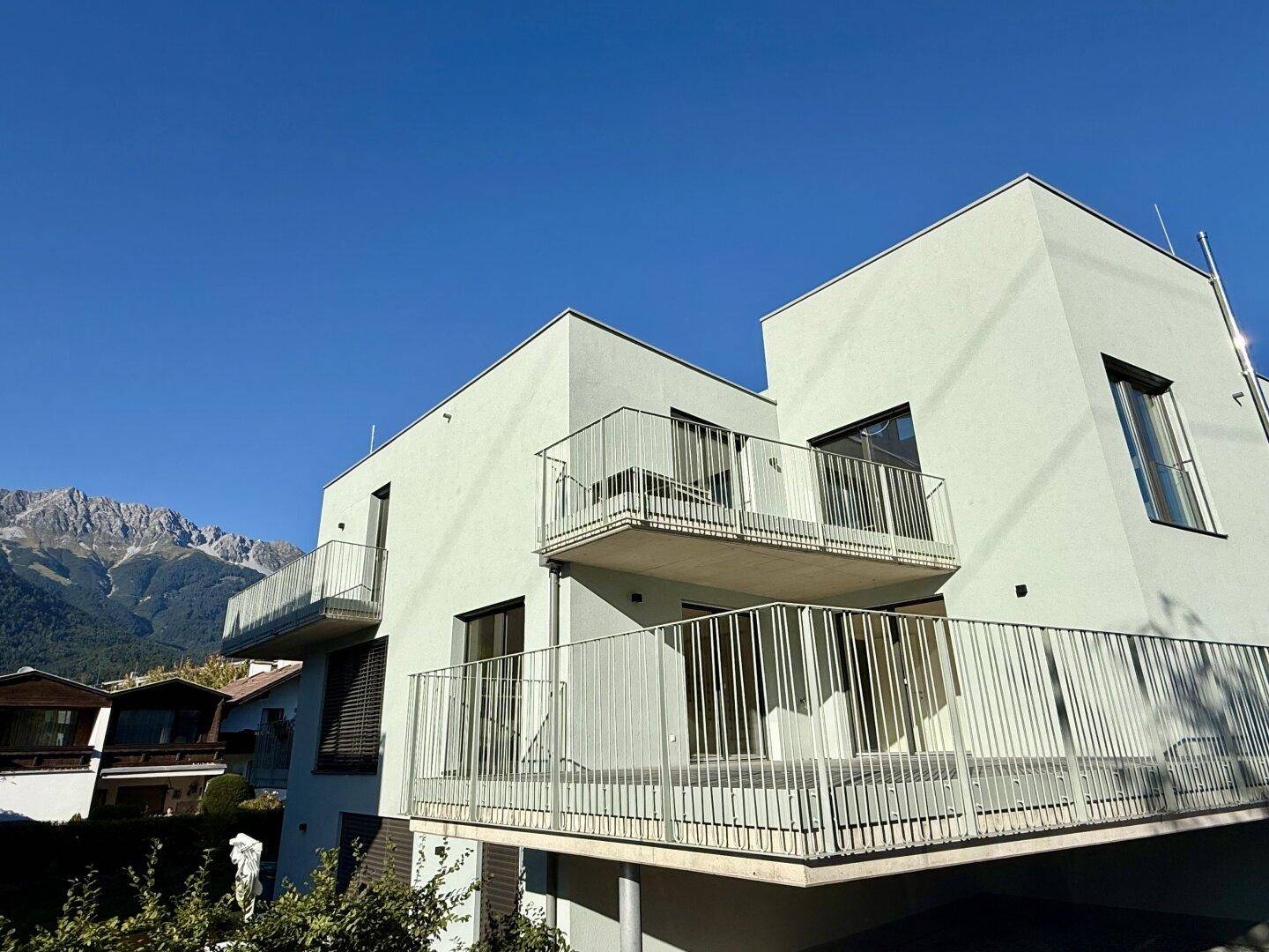 Moderne Architektur mit mehreren Balkonen und einer hellen Fassade vor Bergkulisse.