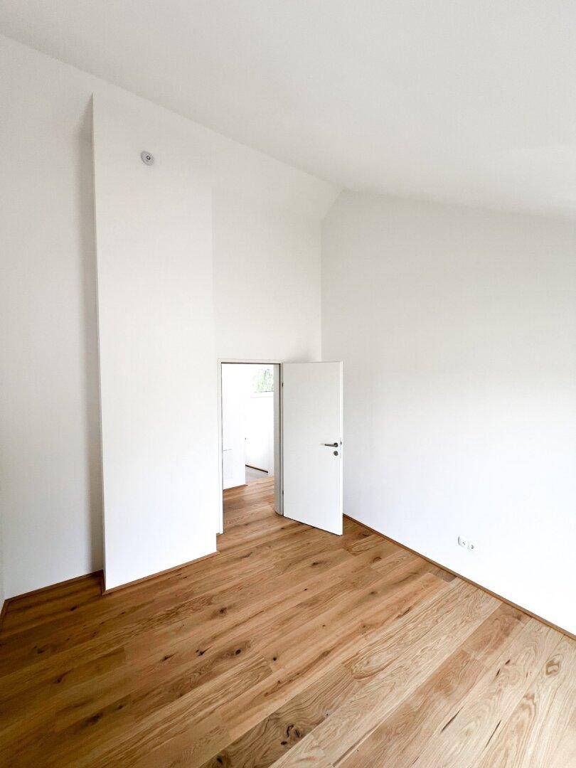 Leeres Zimmer mit Holzboden und weiß gestrichenen Wänden, bereit zur individuellen Gestaltung.