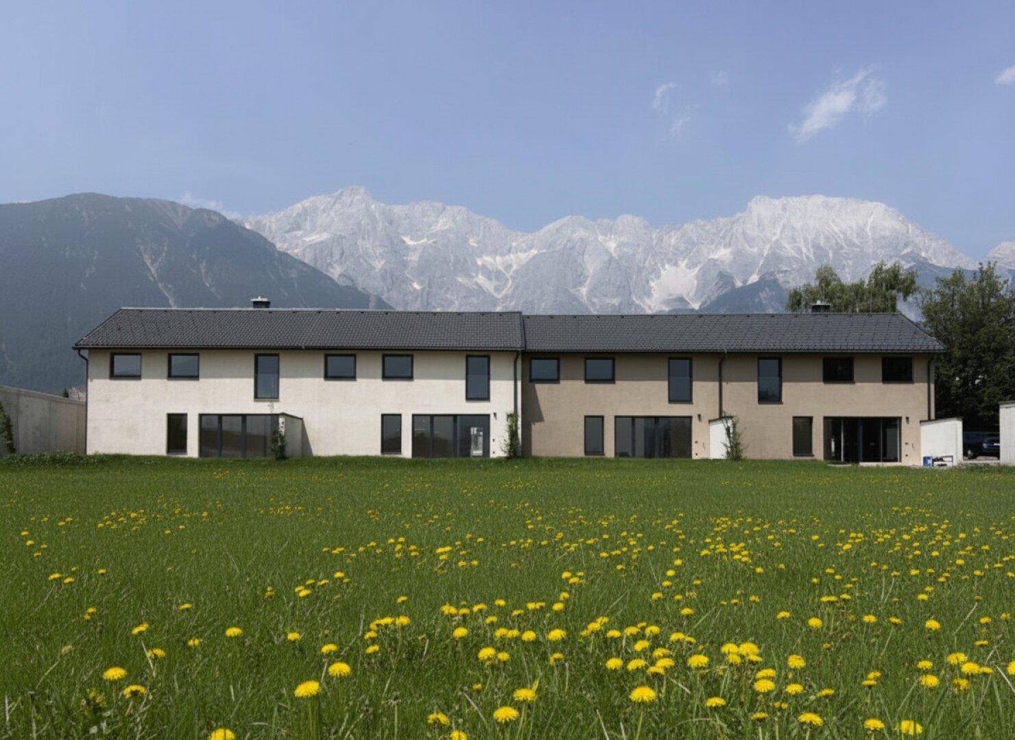 Moderne Reihenhäuser vor einer beeindruckenden Bergkulisse mit grünen Wiesen.