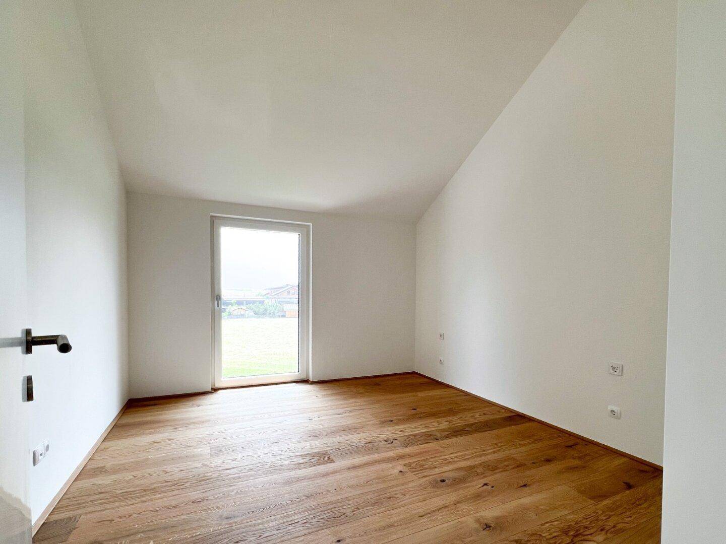Geräumiges Schlafzimmer im Dachgeschoss mit Holzboden und Zugang zu einem möglichen Balkon.