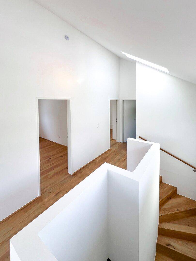 Heller Flur mit Holztreppe, Dachfenster und Zugang zu weiteren Räumen im Obergeschoss.