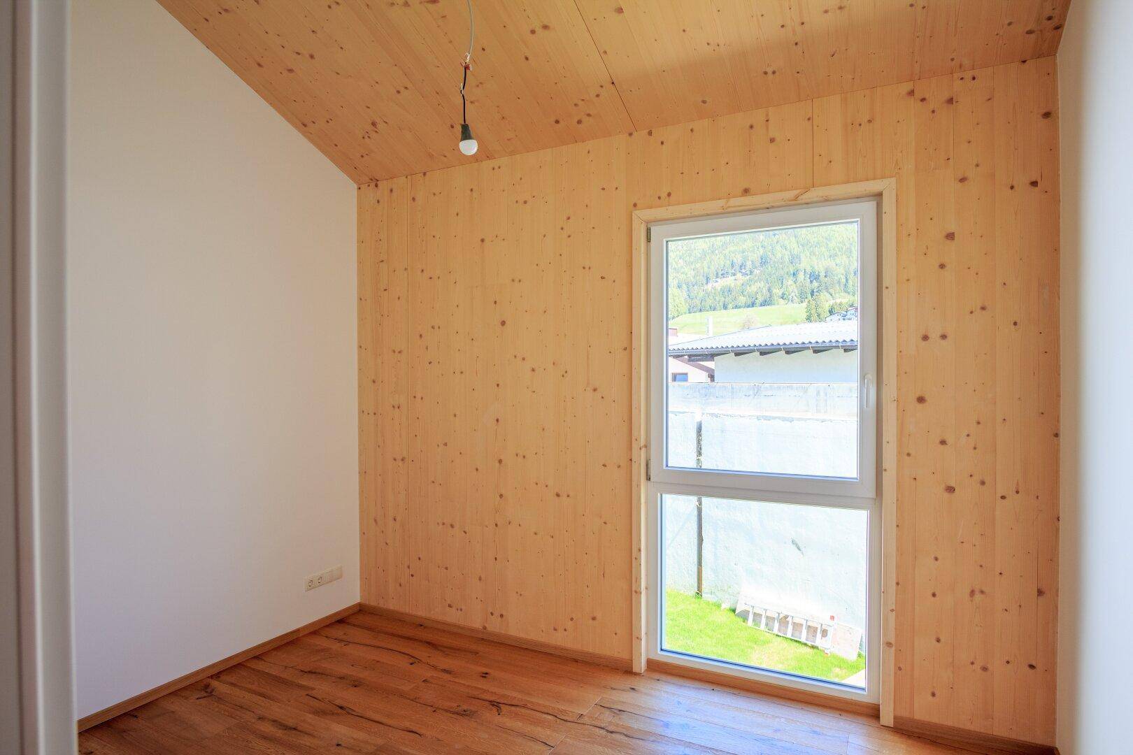 Heller Raum mit Holzwänden, Holzboden und Dachschräge in einem Neubau.