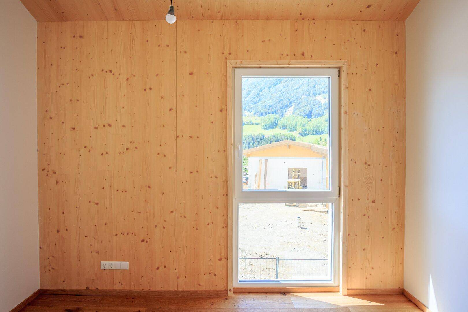 Leerer Raum mit Holzwänden, Holzboden und Fenster mit Blick ins Grüne.
