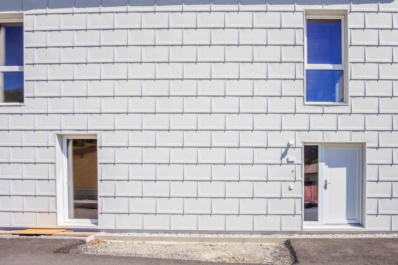 Nahaufnahme der modernen Fassade mit grauen Schindeln und weißen Fenstern.