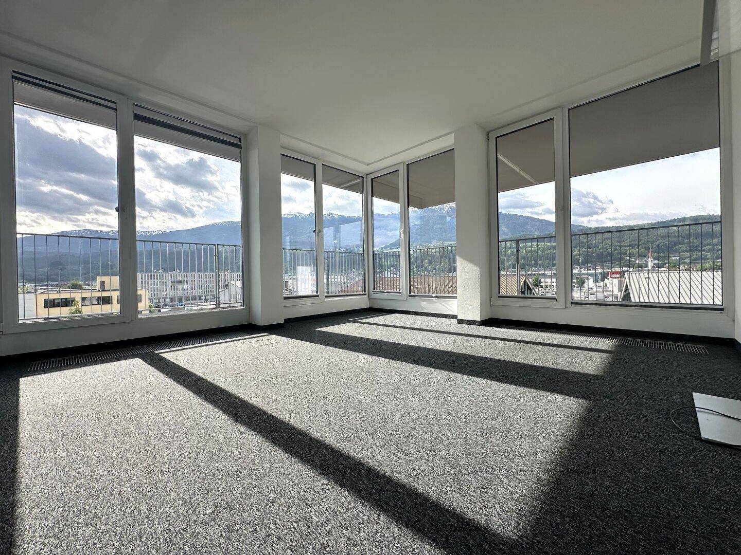 Heller Eckraum mit Teppichboden und großen Fenstern, die einen weiten Blick auf die Berge bieten.
