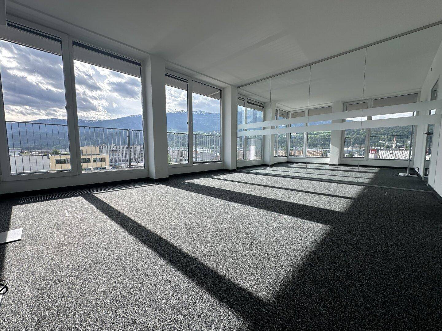 Geräumiger Büroraum mit Teppichboden, großen Fenstern und Panoramablick auf die Berge.