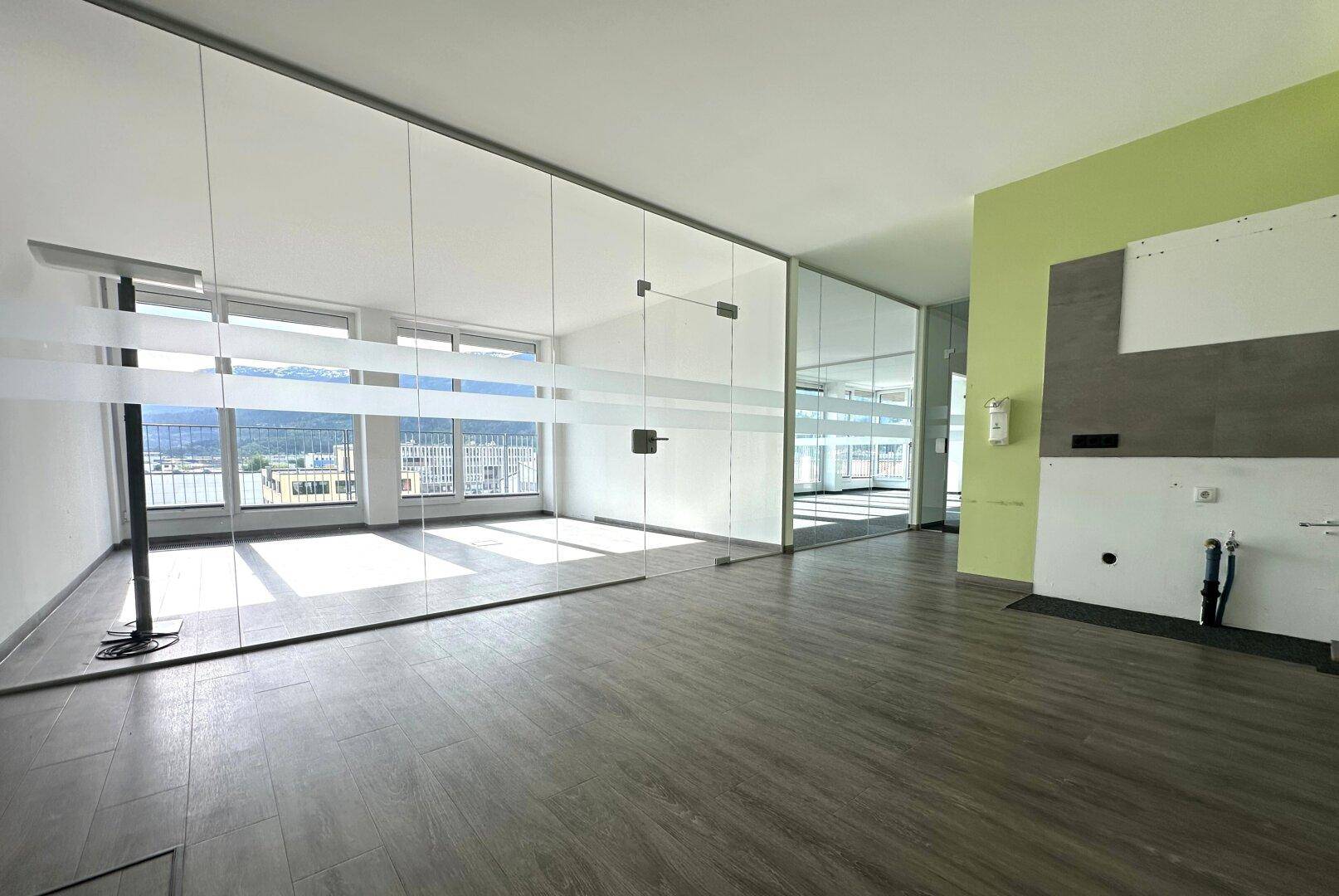 Moderner Büroraum mit Glaswänden, Holzboden und einem Hauch von Grün an der Wand.