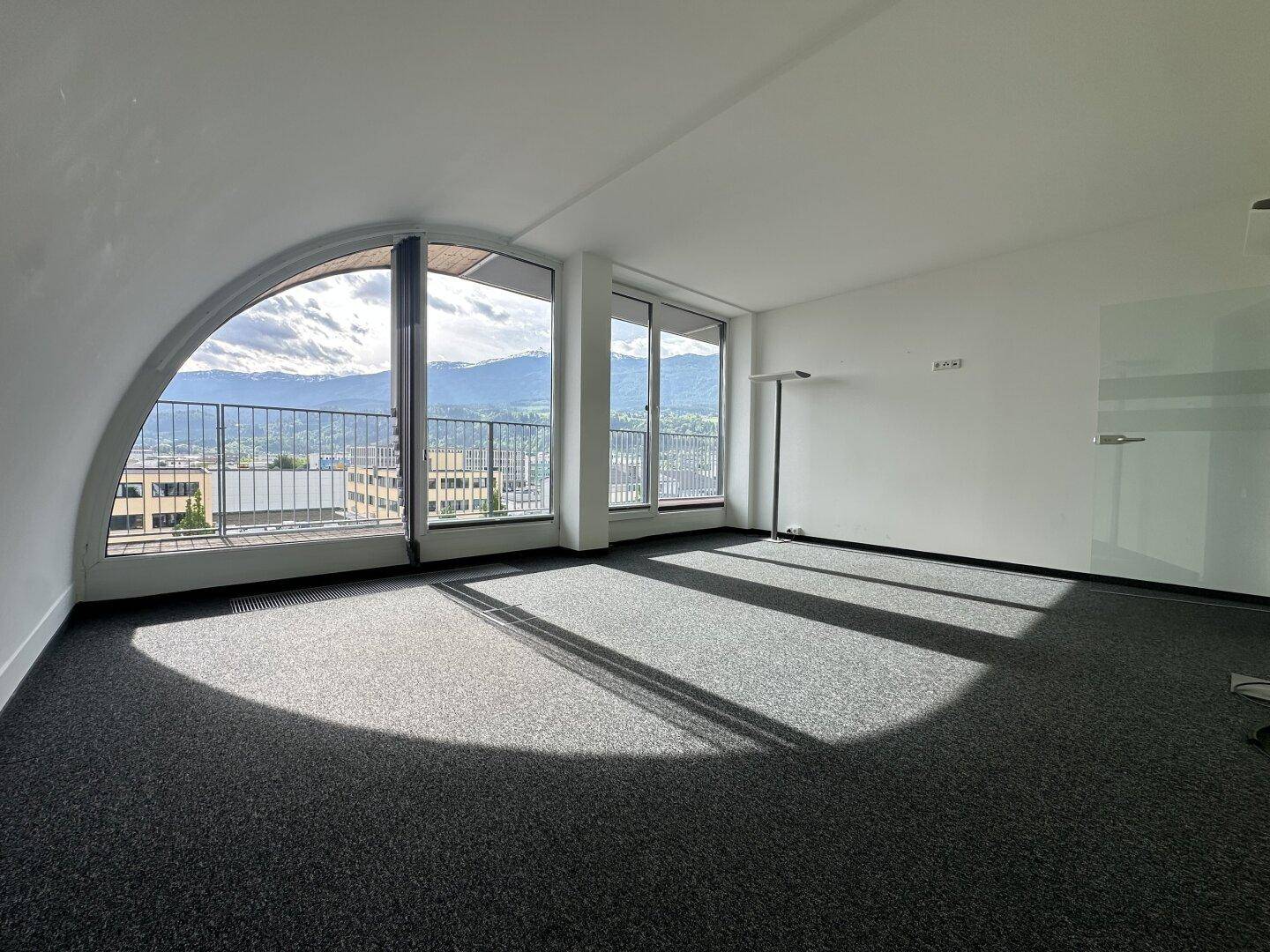Heller Büroraum mit großen Bogenfenstern, Teppichboden und beeindruckendem Bergblick.