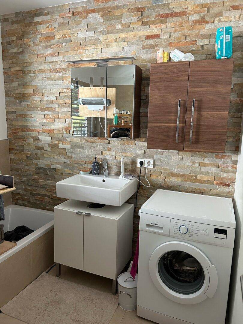 Modernes Badezimmer mit Steinwand, Einzelwaschbecken, Badewanne und Waschmaschine.