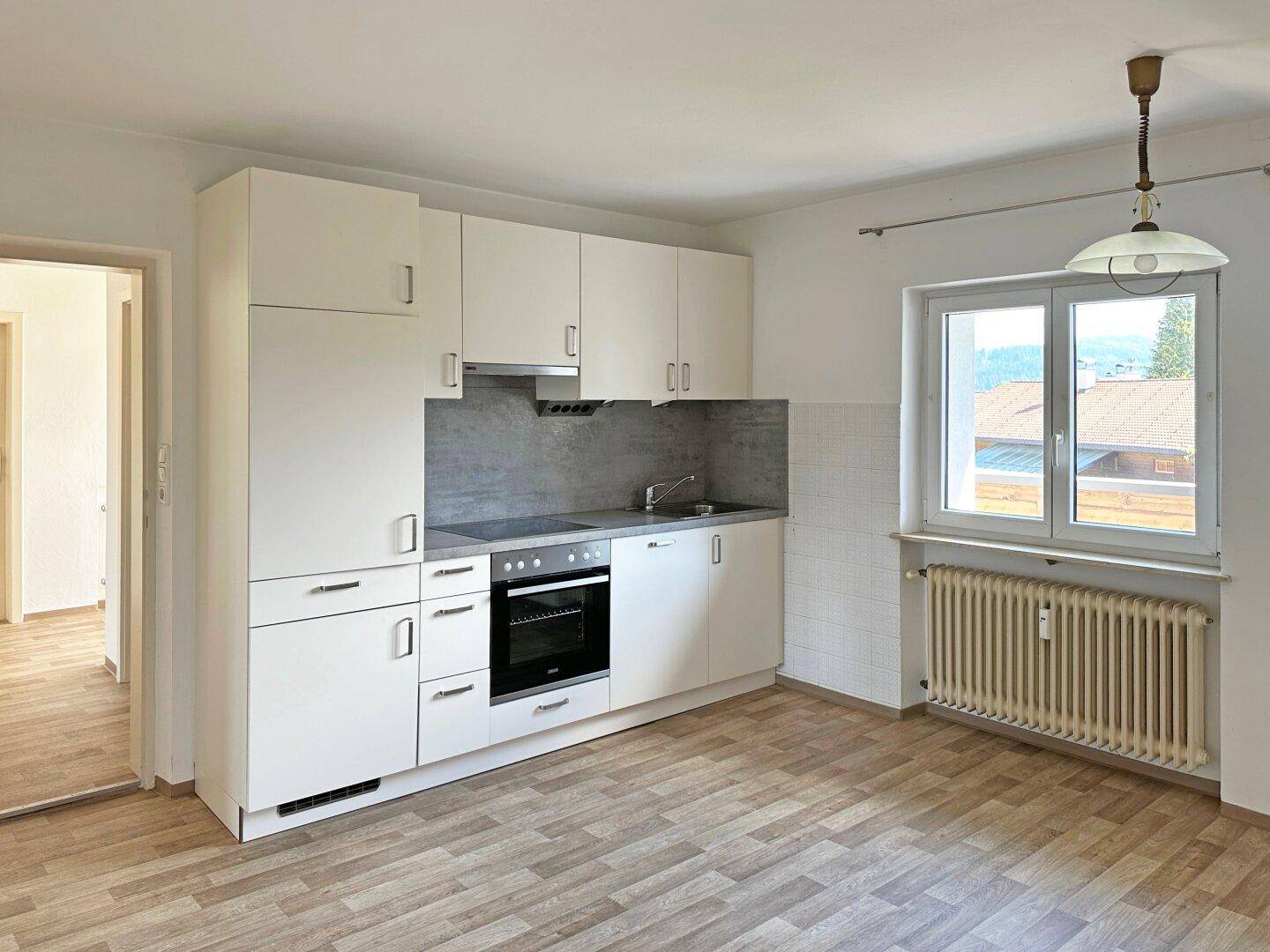 Kleine, funktionale Küche mit weißen Schränken, Einbauherd und Fenster.