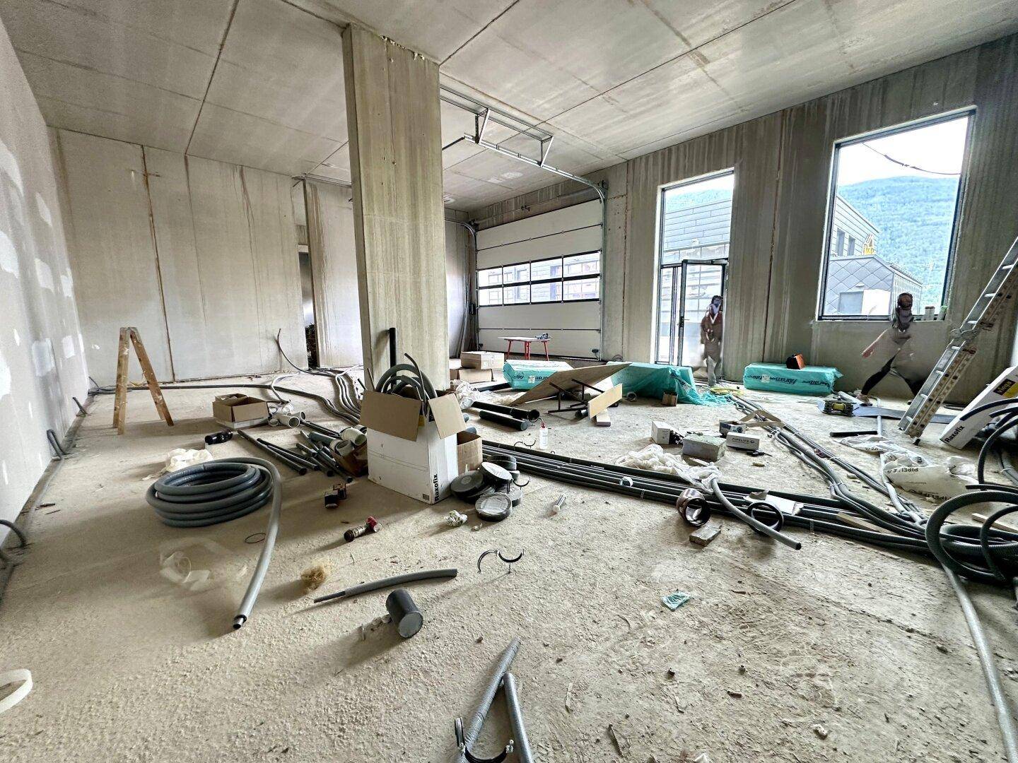 Großer Lagerraum im Rohbau mit Rolltor, Betonwänden und vielen Installationskabeln.