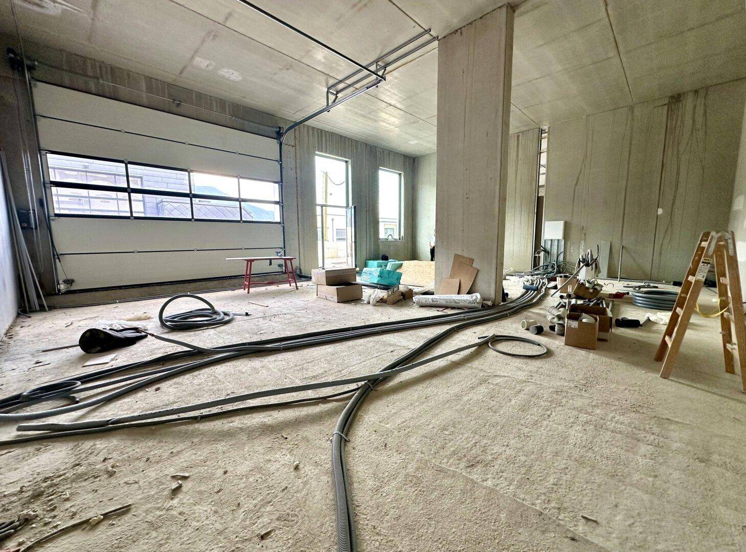 Geräumiger Lagerbereich im Rohbau mit Rolltor, Betonstützen und sichtbaren Installationen.