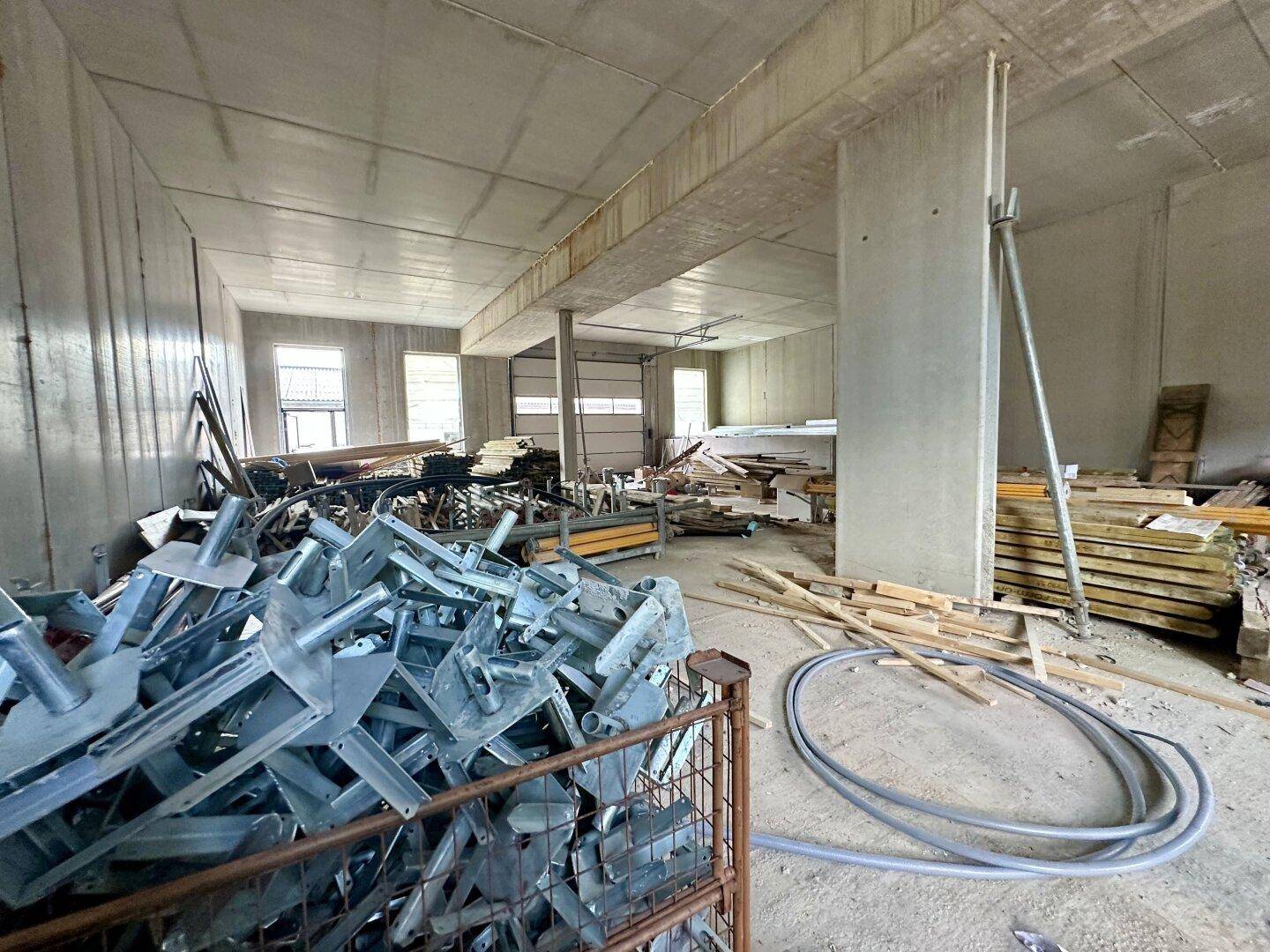 Geräumiger Lagerraum im Rohbau mit Baumaterialien und massiven Betonstützen.
