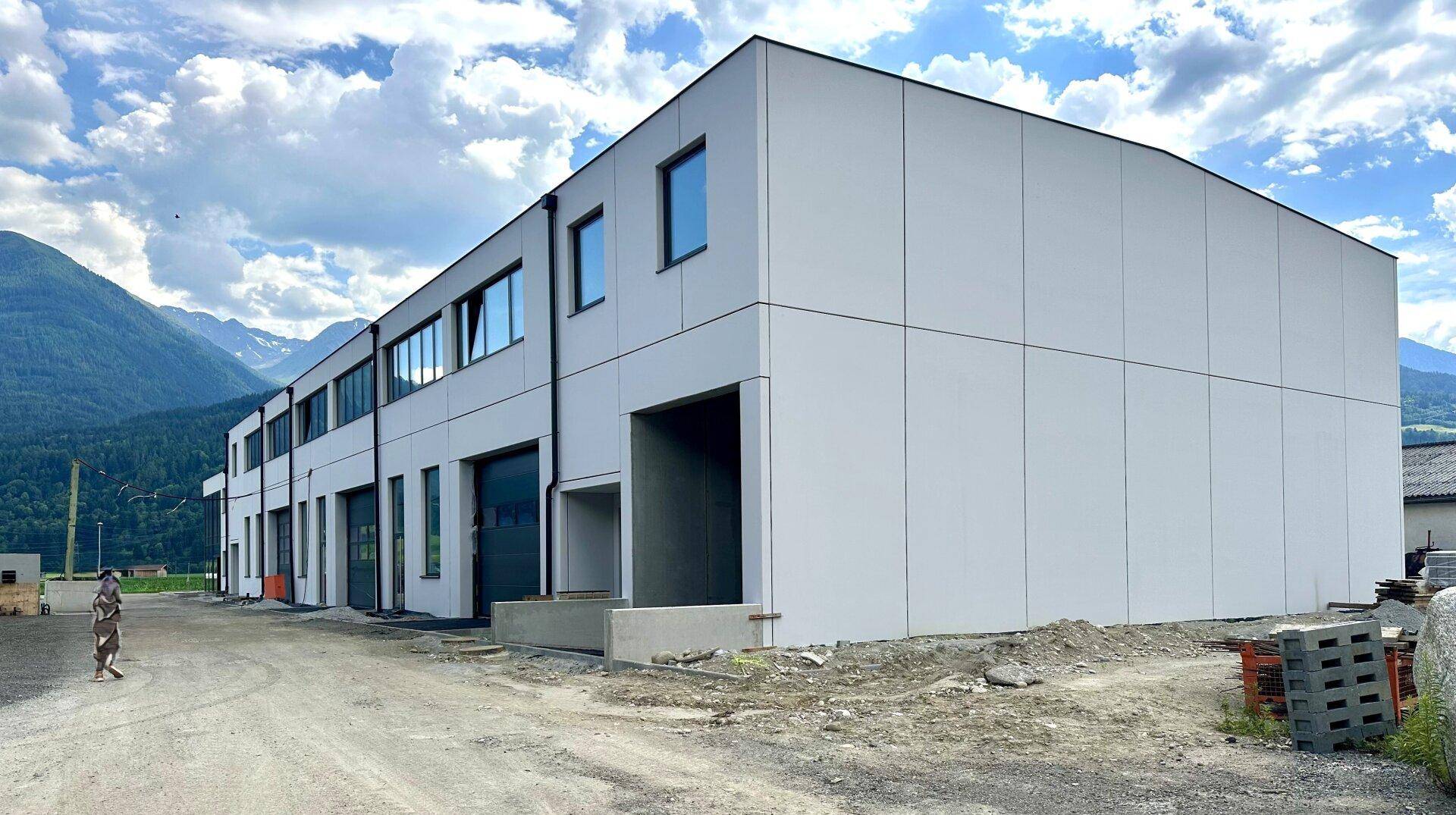 Rückansicht des modernen Neubaus mit schlichter Fassade und Fenstern vor Bergkulisse.