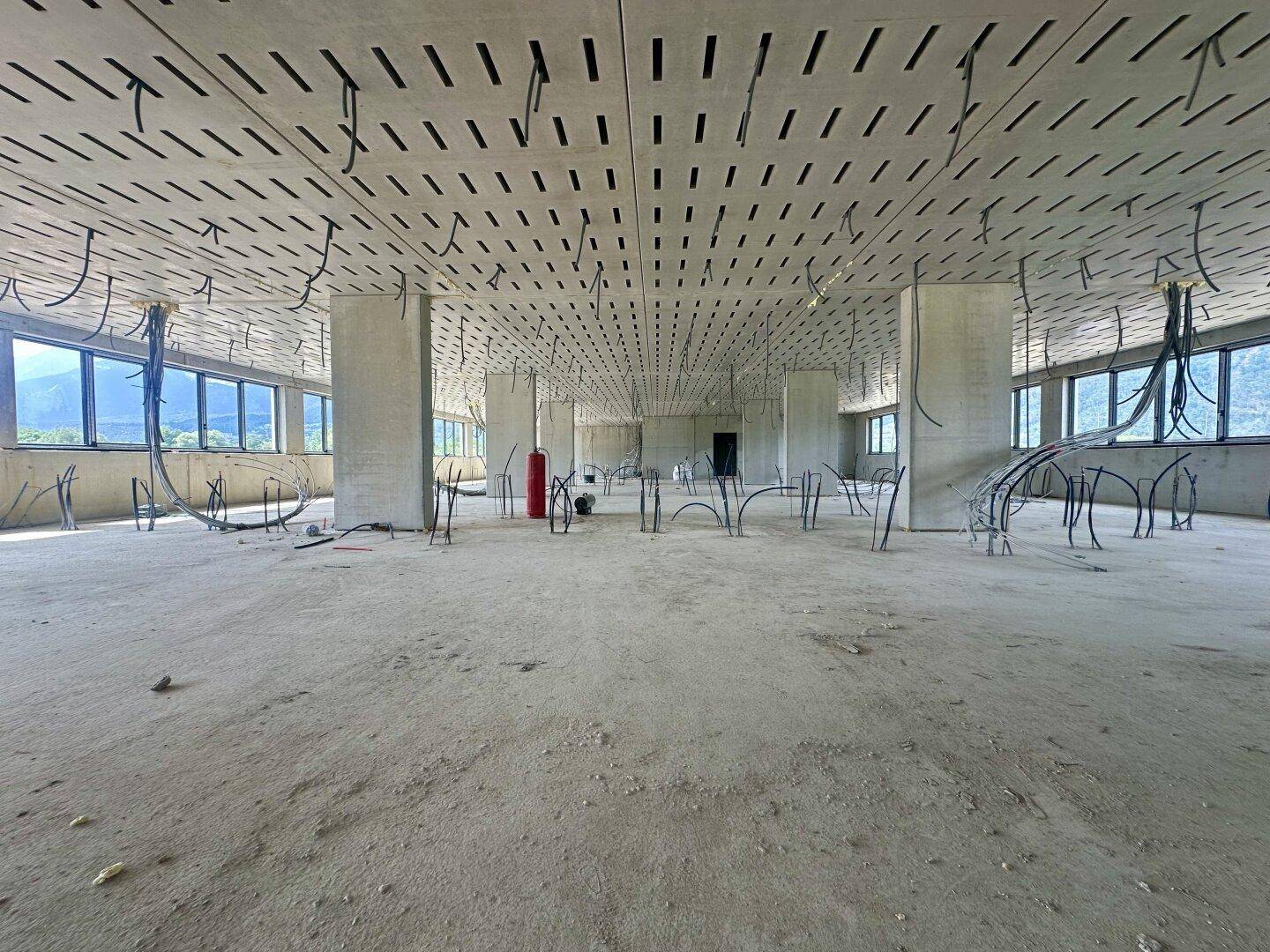Großer, offener Büroraum im Rohbau mit perforierter Decke und vielen Installationskabeln.