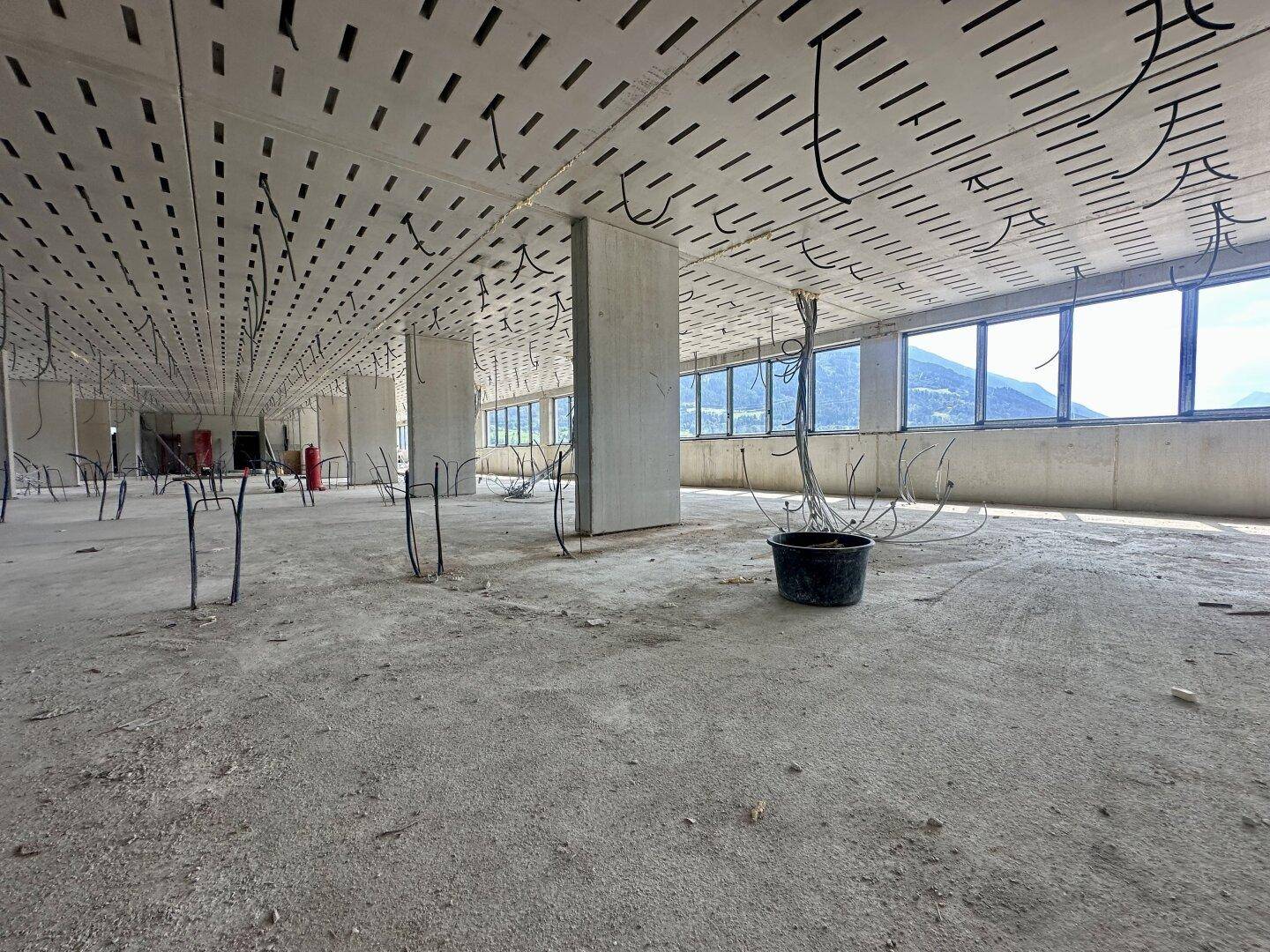 Weiter Bürobereich im Rohbau mit perforierter Decke, Betonstützen und großen Fenstern.