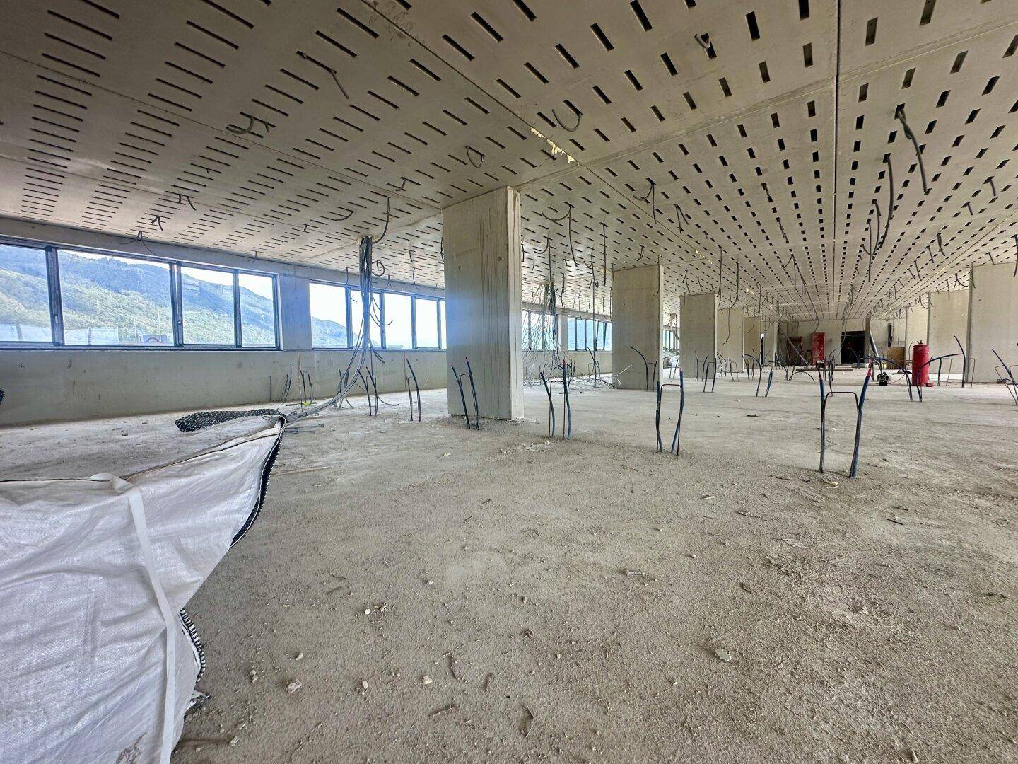 Offener Büroraum im Rohbau mit perforierter Decke, Betonstützen und Installationskabeln.