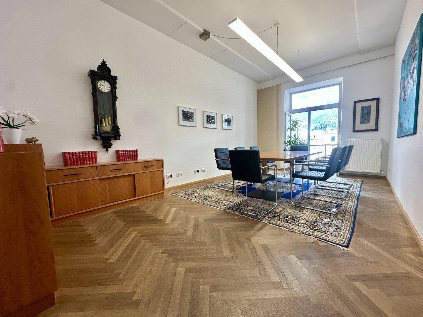Konferenzraum mit großem Holztisch, traditioneller Wanduhr und Fischgrätparkettboden.