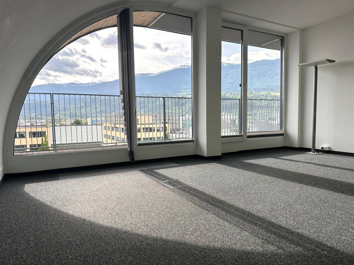 Heller Büroraum mit großen Fenstern, Teppichboden und beeindruckendem Bergblick.