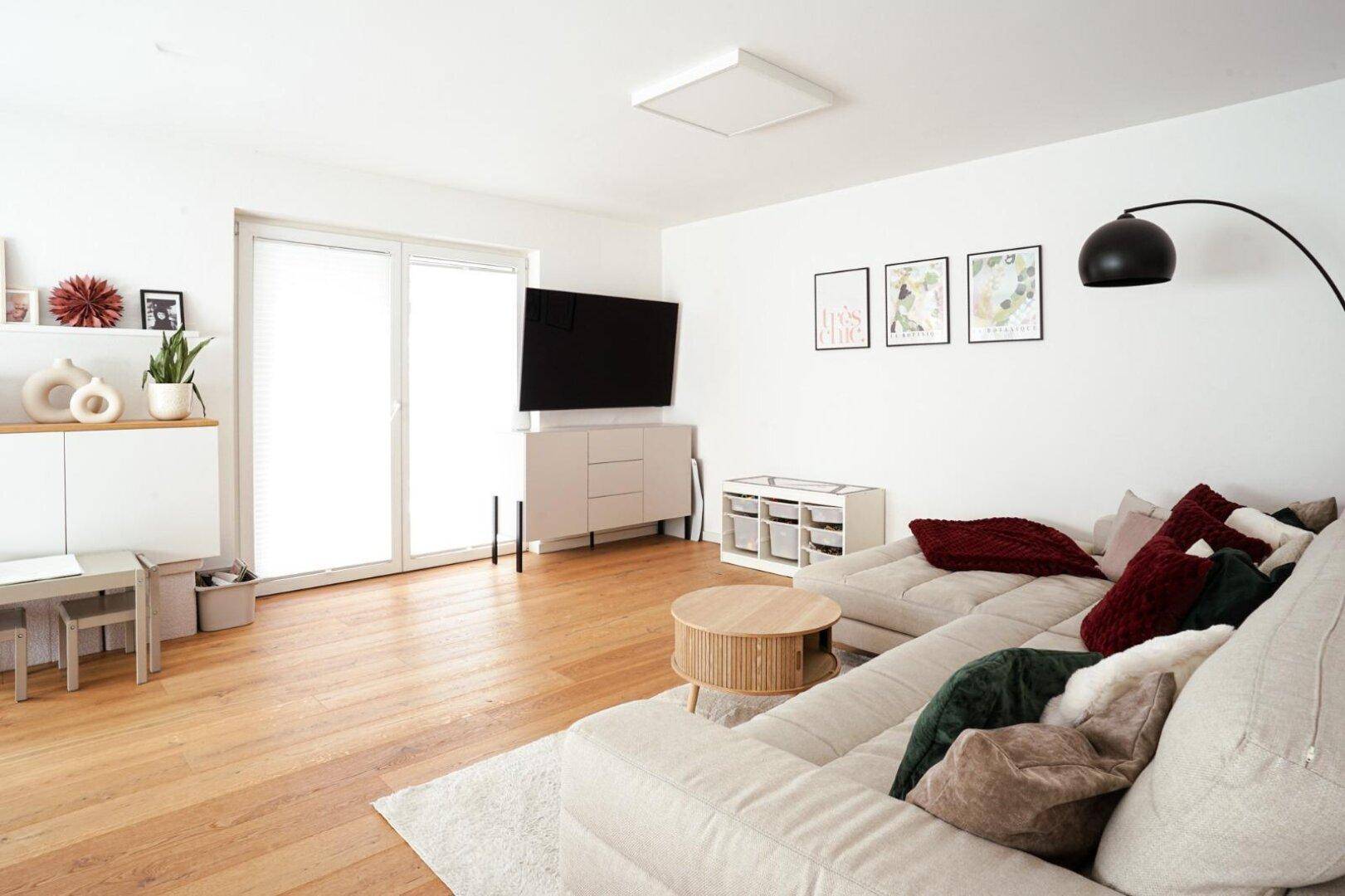 Modernes Wohnzimmer mit großem Ecksofa, Fernseher und hellem Holzboden, gut beleuchtet.