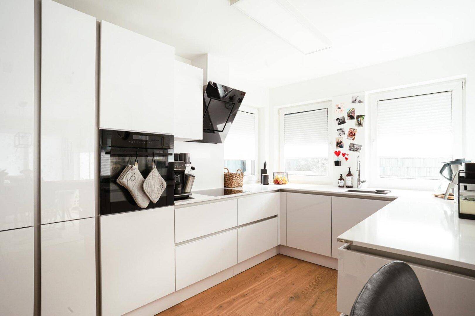 Moderne Küche mit weißen Hochglanzfronten, integriertem Backofen und Induktionskochfeld, hell und funktional.