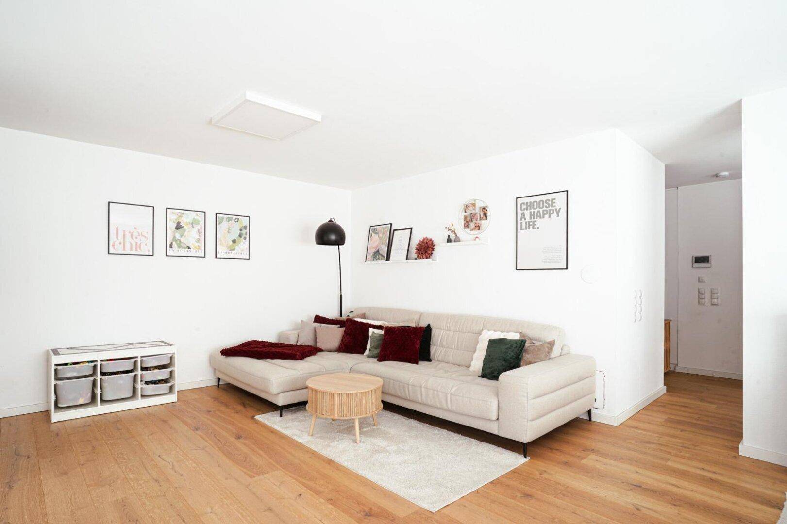 Geräumiges Wohnzimmer mit beigem Ecksofa und stilvoller Wanddekoration, auf hellem Holzboden.