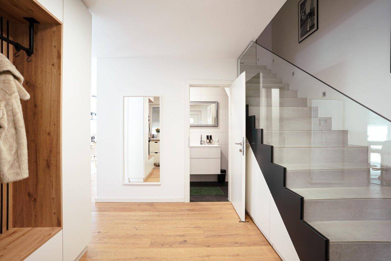 Moderner Flur mit eleganter Treppe und Glasgeländer, führt zu weiteren Räumen.