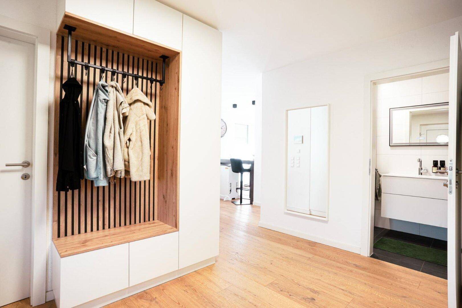 Heller Eingangsbereich mit integrierter Garderobe und Holzboden, Zugang zu einem Badezimmer.