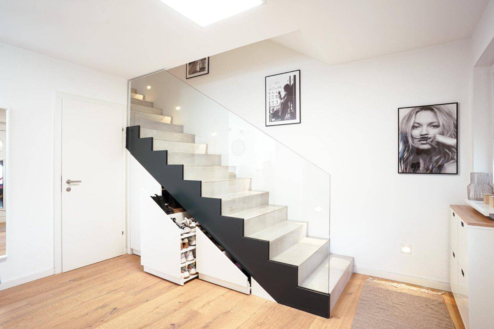 Stilvolle Treppe mit Glasgeländer und cleverem Stauraum darunter, auf hellem Holzboden.