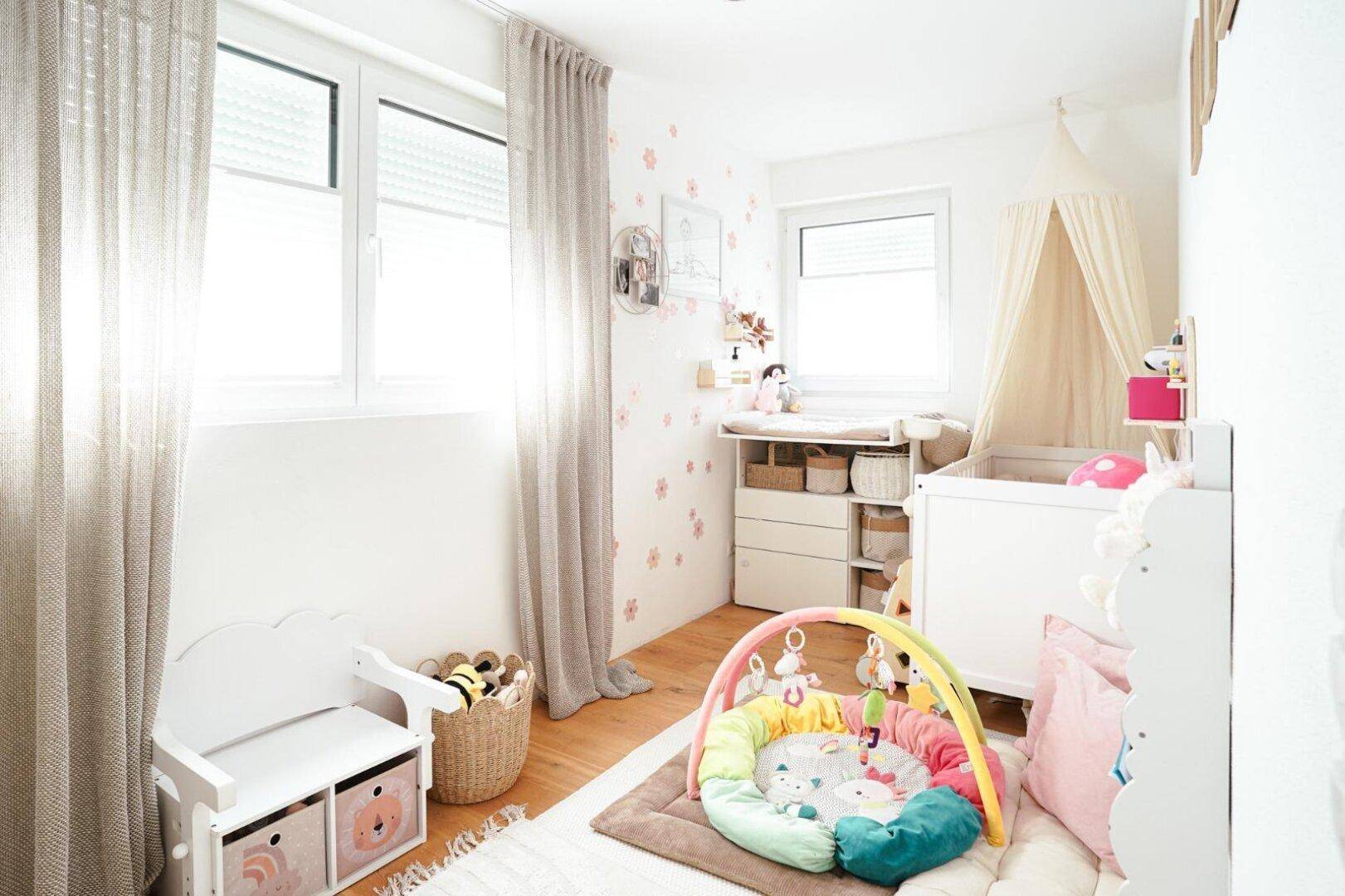 Freundliches Kinderzimmer mit Babybett, Wickeltisch und Spielbereich, hell und liebevoll eingerichtet.