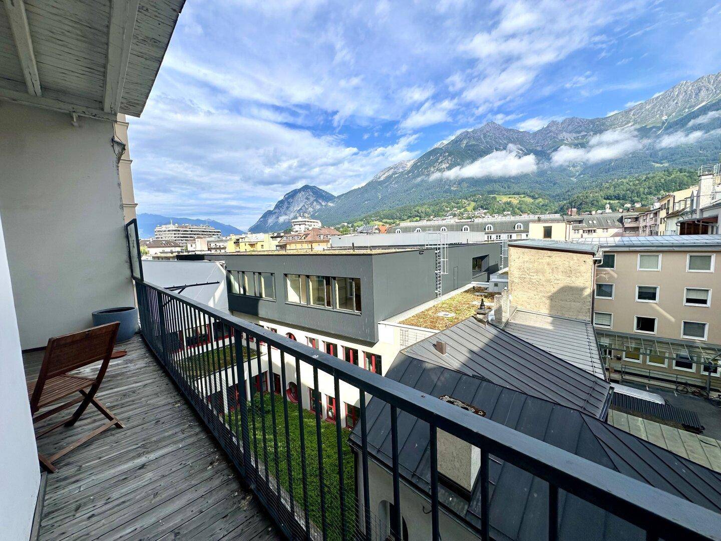 Langer Balkon mit Holzboden und Metallgeländer, bietet weitreichenden Blick auf die Stadt und Berge.