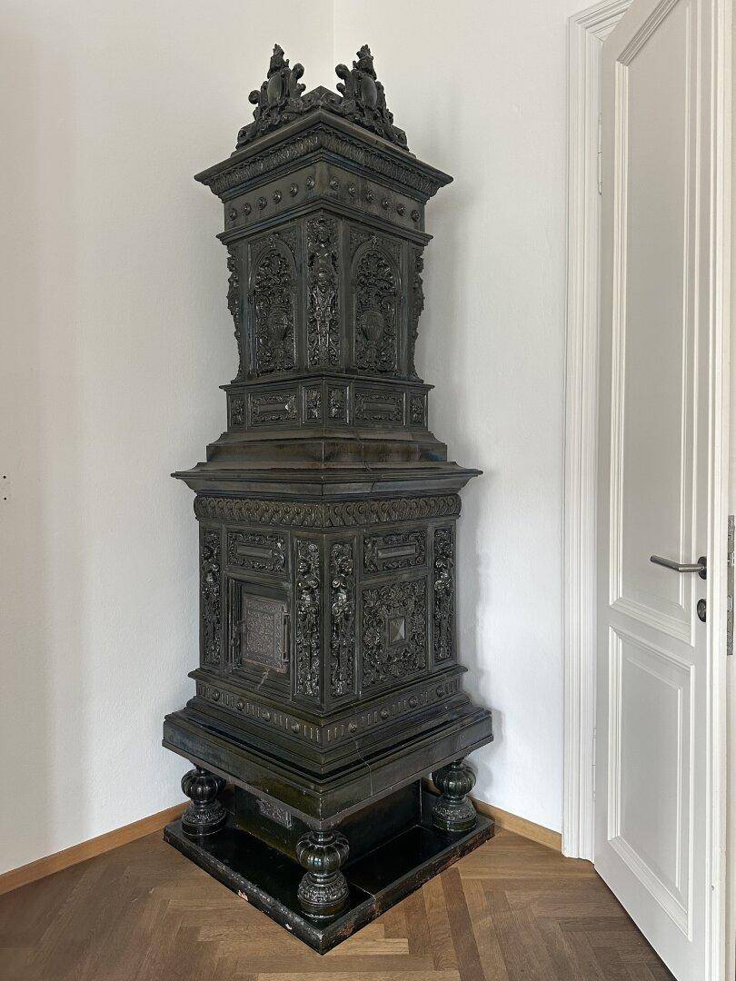 Detailaufnahme eines kunstvoll verzierten, historischen Kachelofens in dunklem Design, der den Raum schmückt.