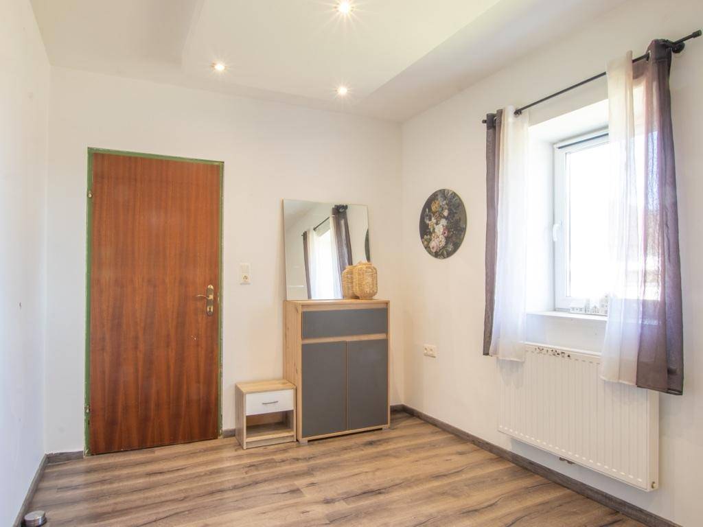 Helles Zimmer mit Laminatboden, Fenster und einem kleinen Schrank mit Spiegel.