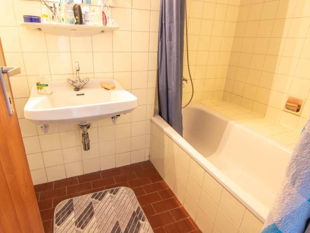 Klassisches Badezimmer mit gelben Fliesen, Badewanne mit Duschvorhang und einem Waschbecken.