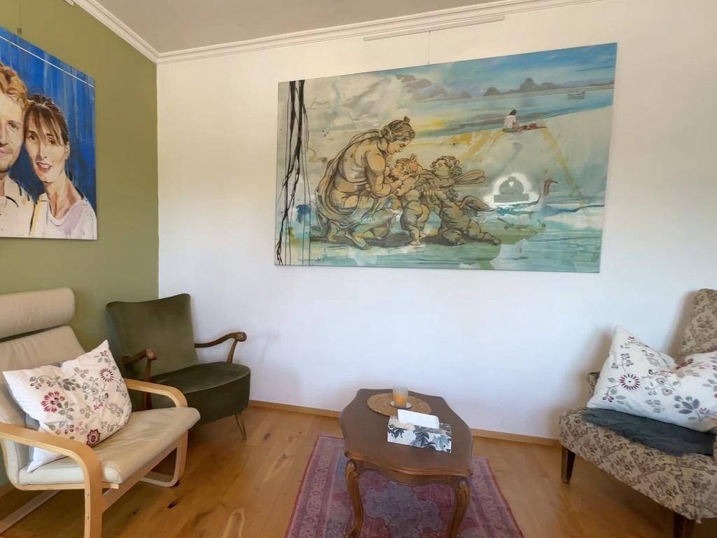 Gemütlicher Wohnbereich mit Sesseln, Couchtisch und Kunstwerken an den Wänden.