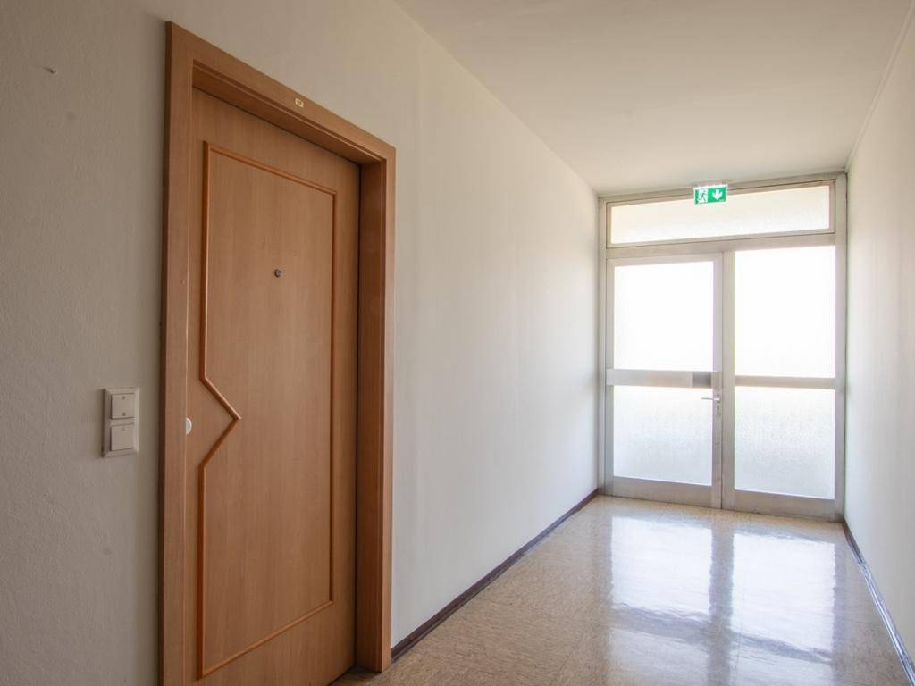 Langer Flur mit heller Tür und Ausgang zu einem Gemeinschaftsbereich.