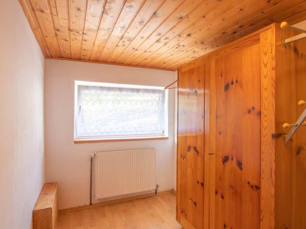 Kleines Zimmer mit Holzschrank, Holzdecke und einem Fenster, das Tageslicht hereinlässt.