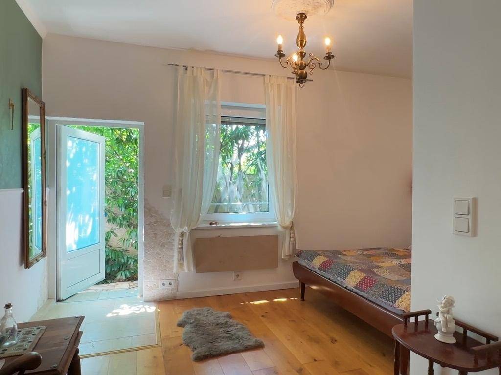 Helles Schlafzimmer mit Holzboden, Fenster und Zugang zu einem Außenbereich.