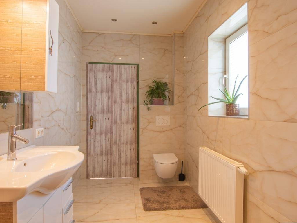 Helles Badezimmer mit wandhängendem WC, Fenster und Heizkörper, komplett gefliest.