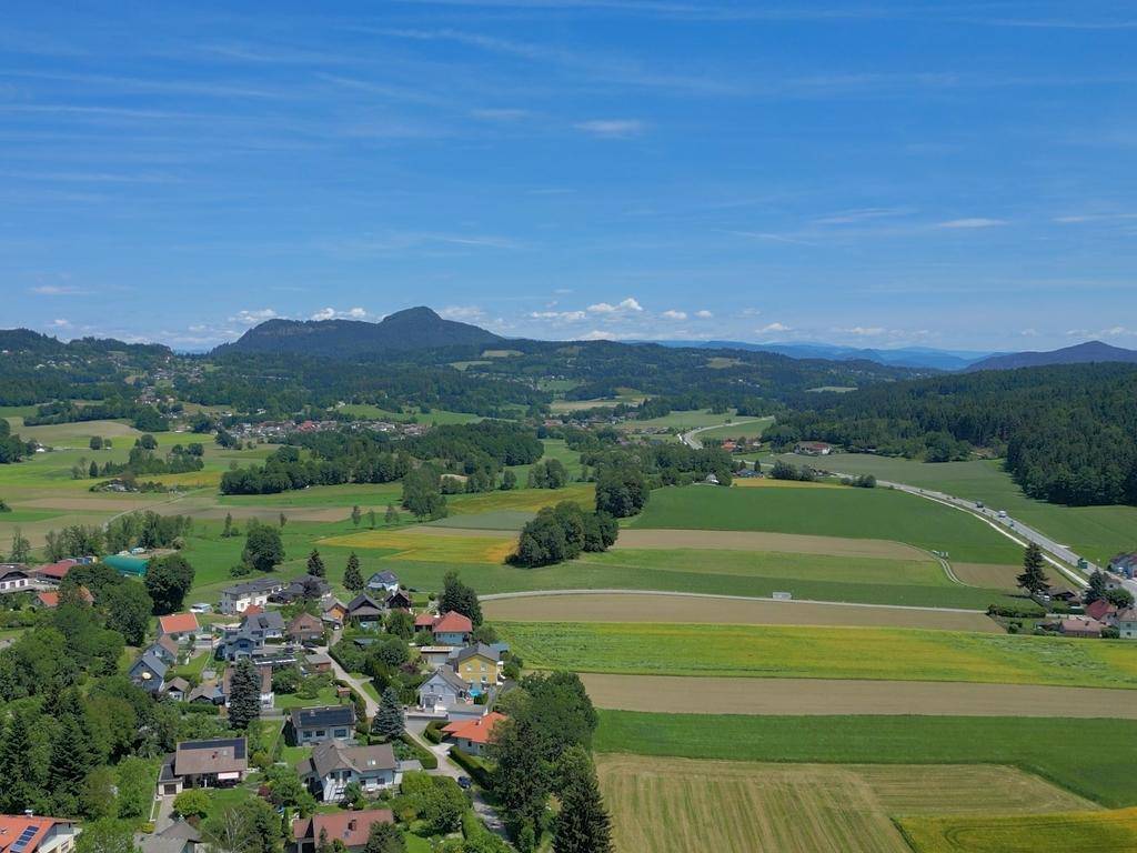 Panoramablick aus der Luft auf ein Dorf, weite Felder und majestätische Berge unter klarem Himmel.
