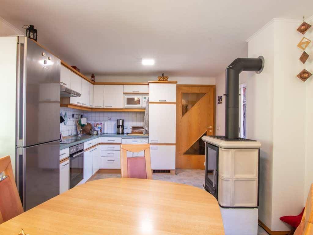 Funktionale Küche mit weißen Schränken, Esstisch und einem Kaminofen im Landhausstil.