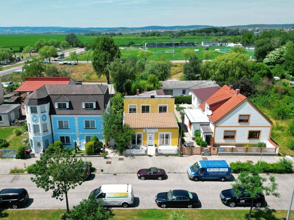 Luftaufnahme einer Wohnsiedlung mit gelbem Haus, umgeben von grünen Feldern und Bäumen.