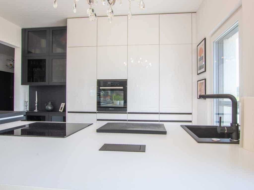 Elegante, moderne Küche mit weißen Schränken, integrierten Geräten und schwarzer Arbeitsplatte.