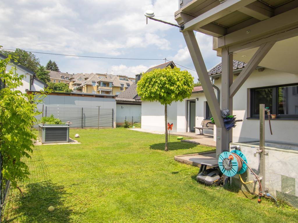 Gepflegter Garten mit Rasenfläche, Bäumen und einem Hochbeet neben dem Haus.