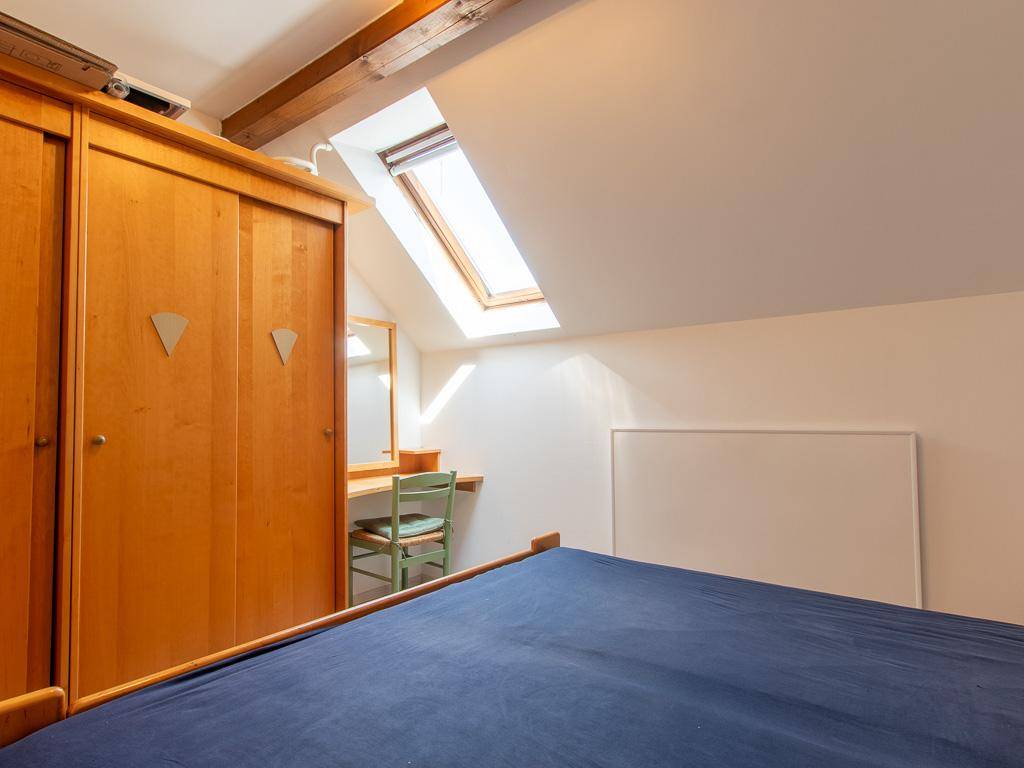 Schlafzimmer im Dachgeschoss mit Holzkleiderschrank, Bett und Dachfenster.